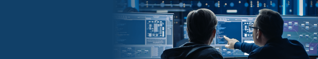 Two men in suits working in front of multiple complex screens. One man points to a screen.