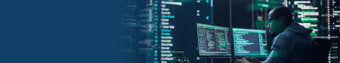 man in a hoodie at a desk working on computers 